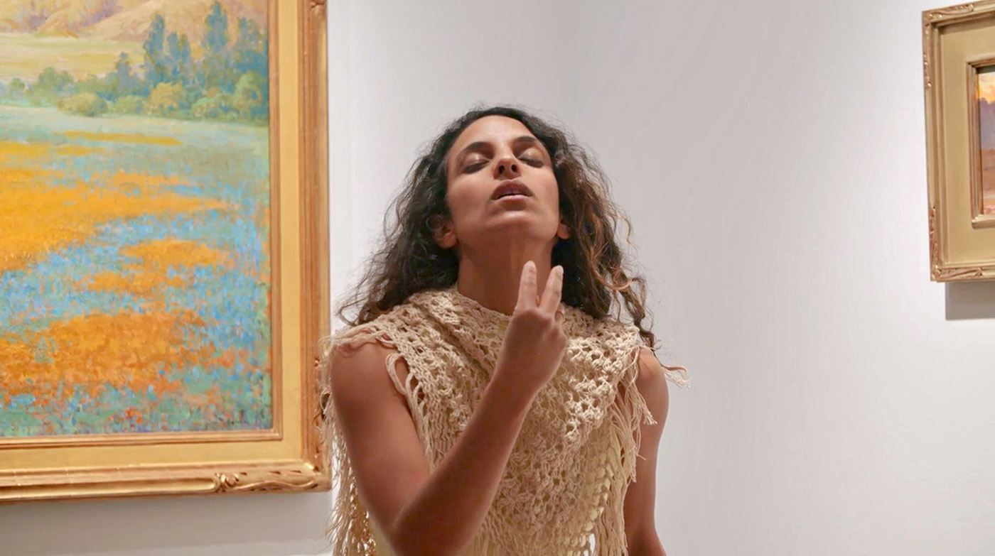 woman standing between two paintings and gesturing with her hands