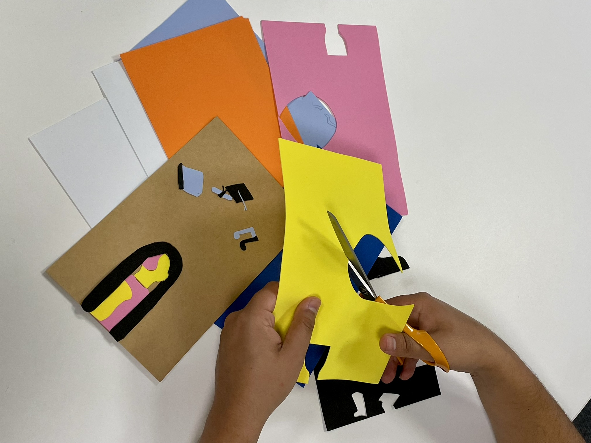 A pair of hands cut a sheet of yellow craft foam. More sheets of craft foam are visible beneath them.